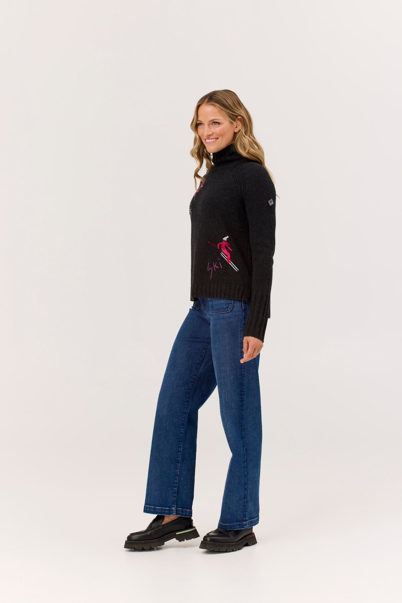 Woman wearing a black turtleneck with a red design and blue jeans on a white background