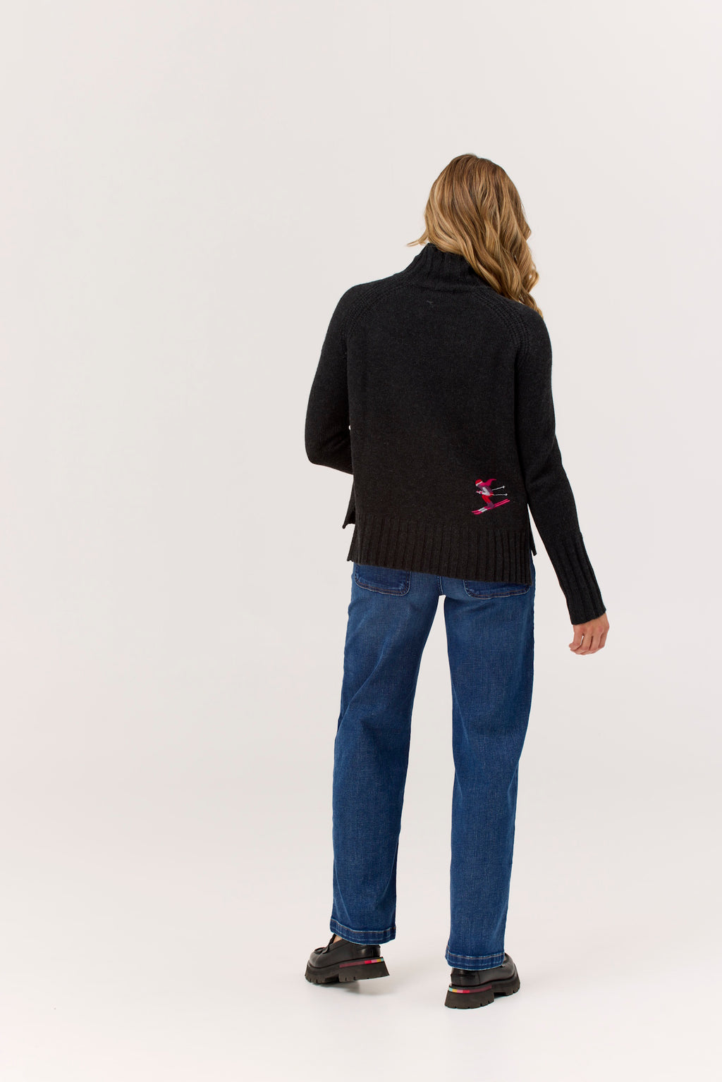 Person wearing a black sweater with a red logo and blue jeans on a white background
