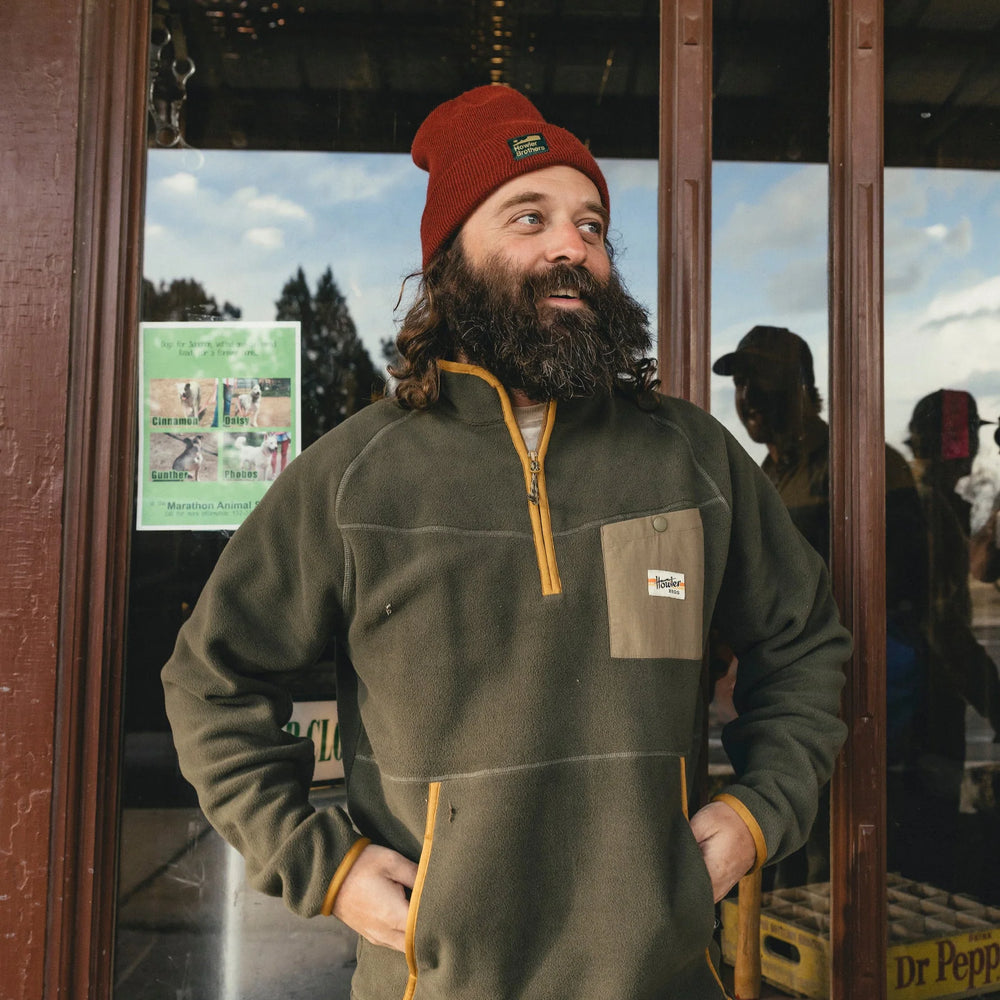 Man wearing a green jacket and red beanie standing in front of a store entrance.