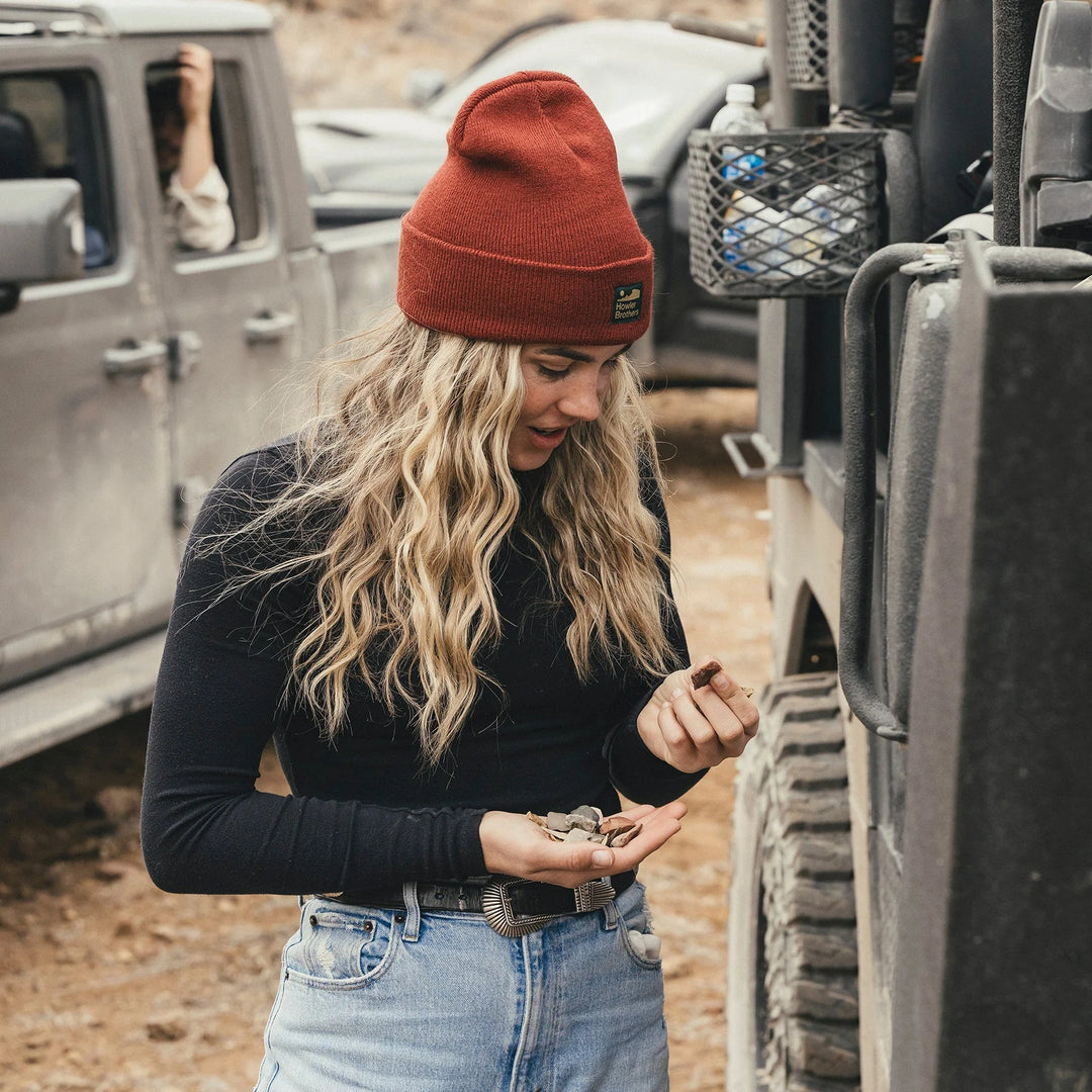 Woman in a red beanie and black sweater standing next to a vehicle in an outdoor setting