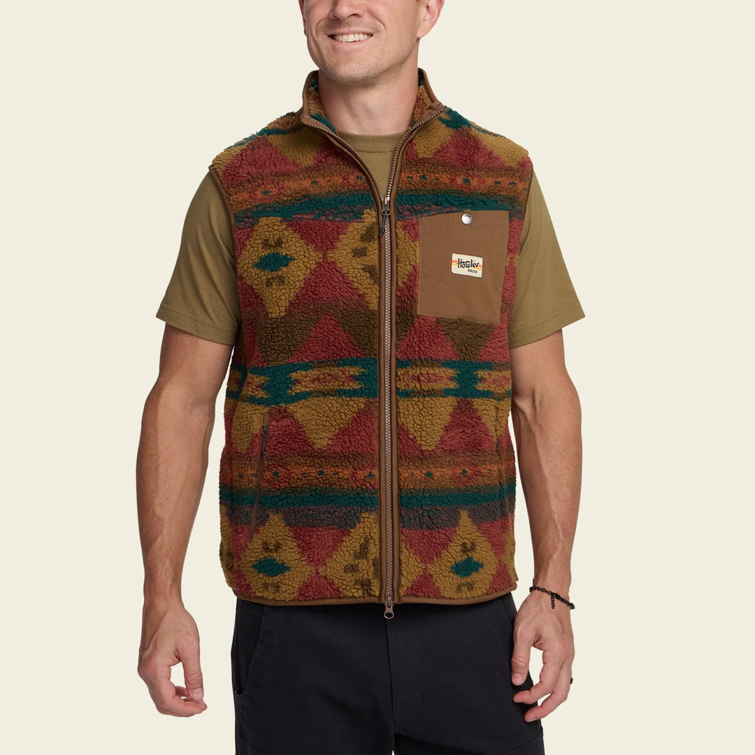 Man wearing a patterned vest with a visible brand logo on a beige background