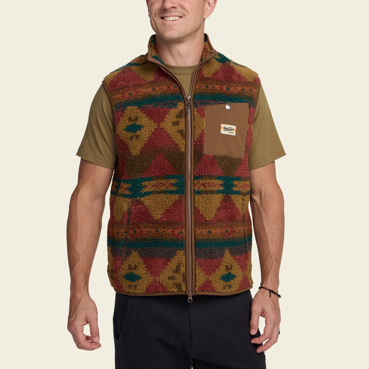 Man wearing a patterned vest with a visible brand logo on a beige background