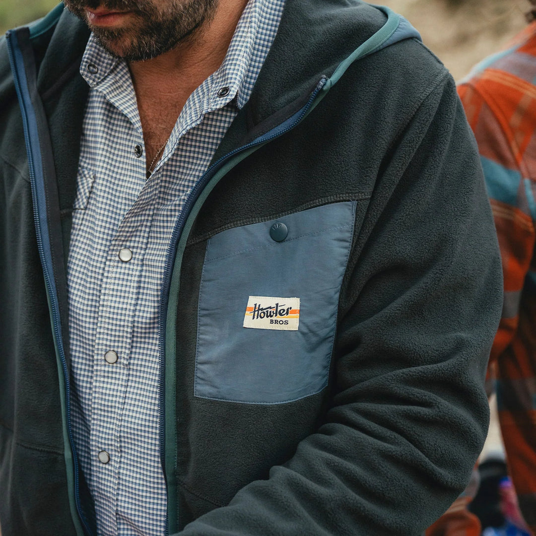 Person wearing a jacket with a Howler Bros logo, standing outdoors.