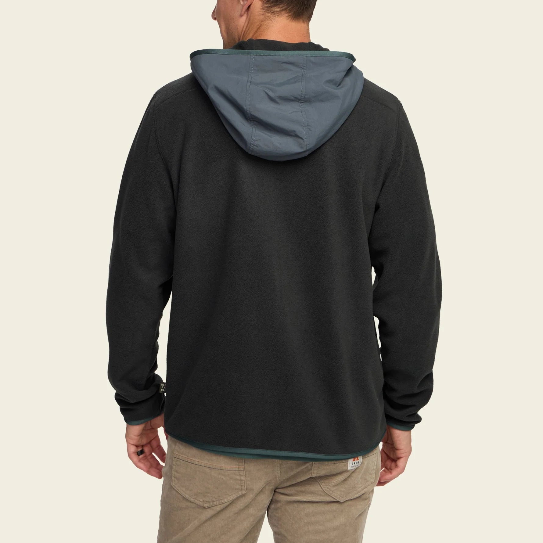 Person wearing a black hoodie with a gray hood on a beige background