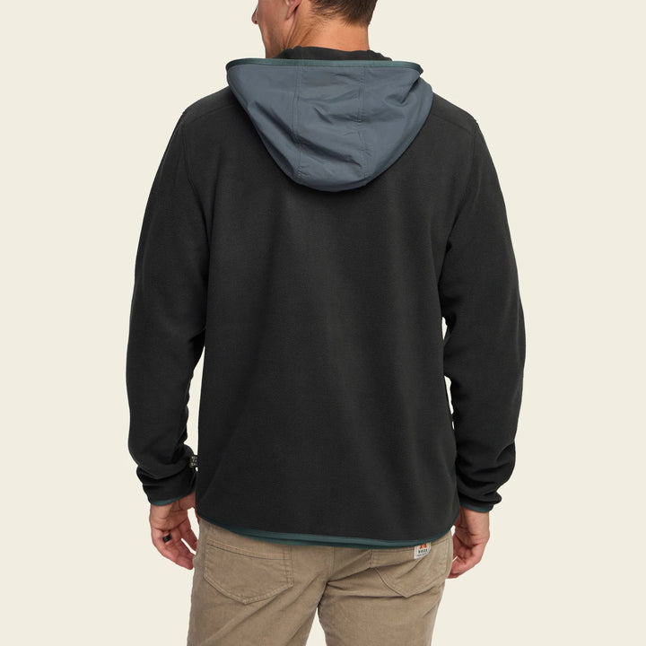 Person wearing a black hoodie with a gray hood on a beige background