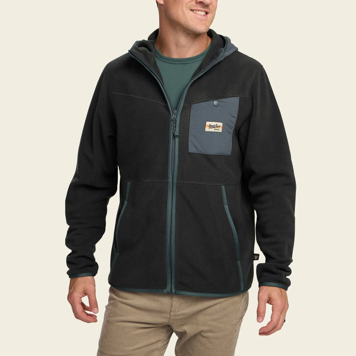 Man wearing a black jacket with a brand logo on a beige background