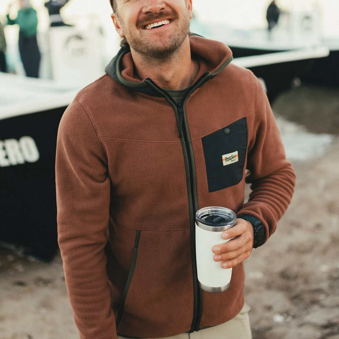 Man wearing a brown jacket holding a white tumbler with a blurred background
