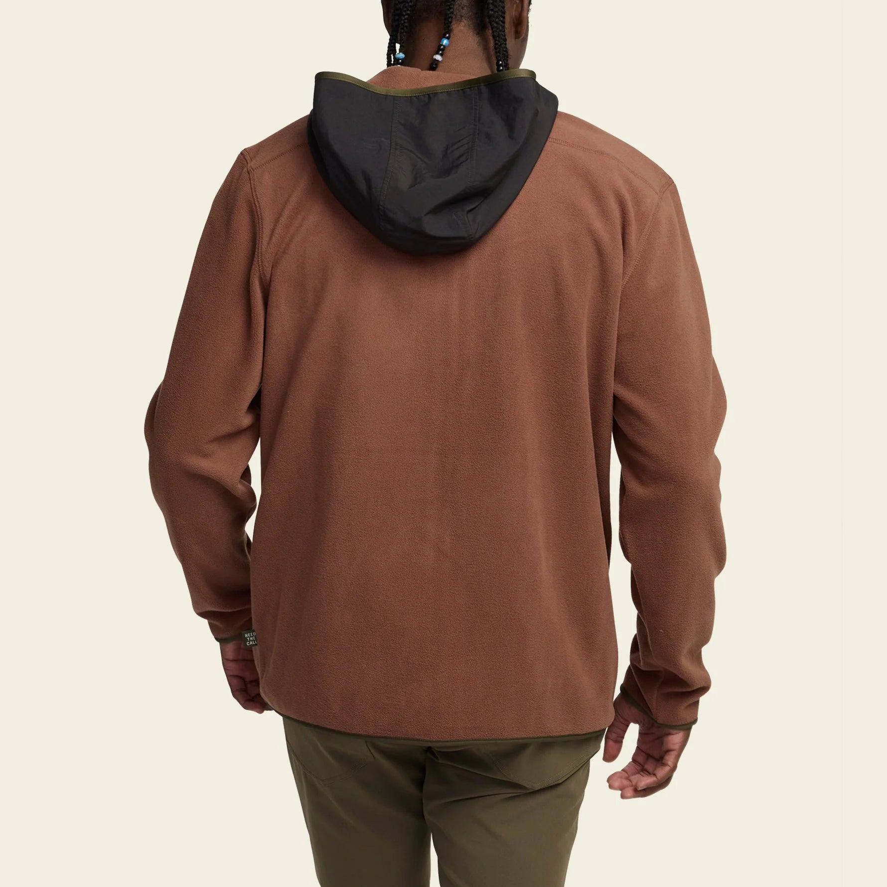 Person wearing a brown hoodie with a black hood on a beige background