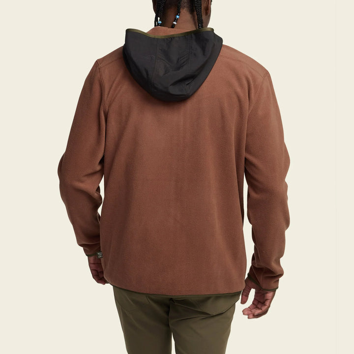 Person wearing a brown hoodie with a black hood on a beige background