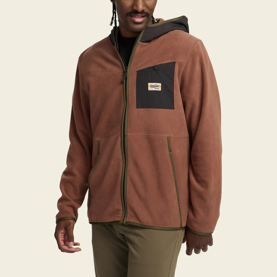 Man wearing a brown jacket with a brand logo on a beige background