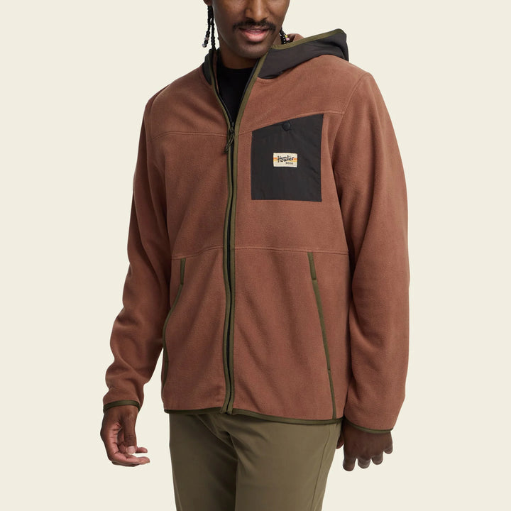 Man wearing a brown jacket with a brand logo on a beige background
