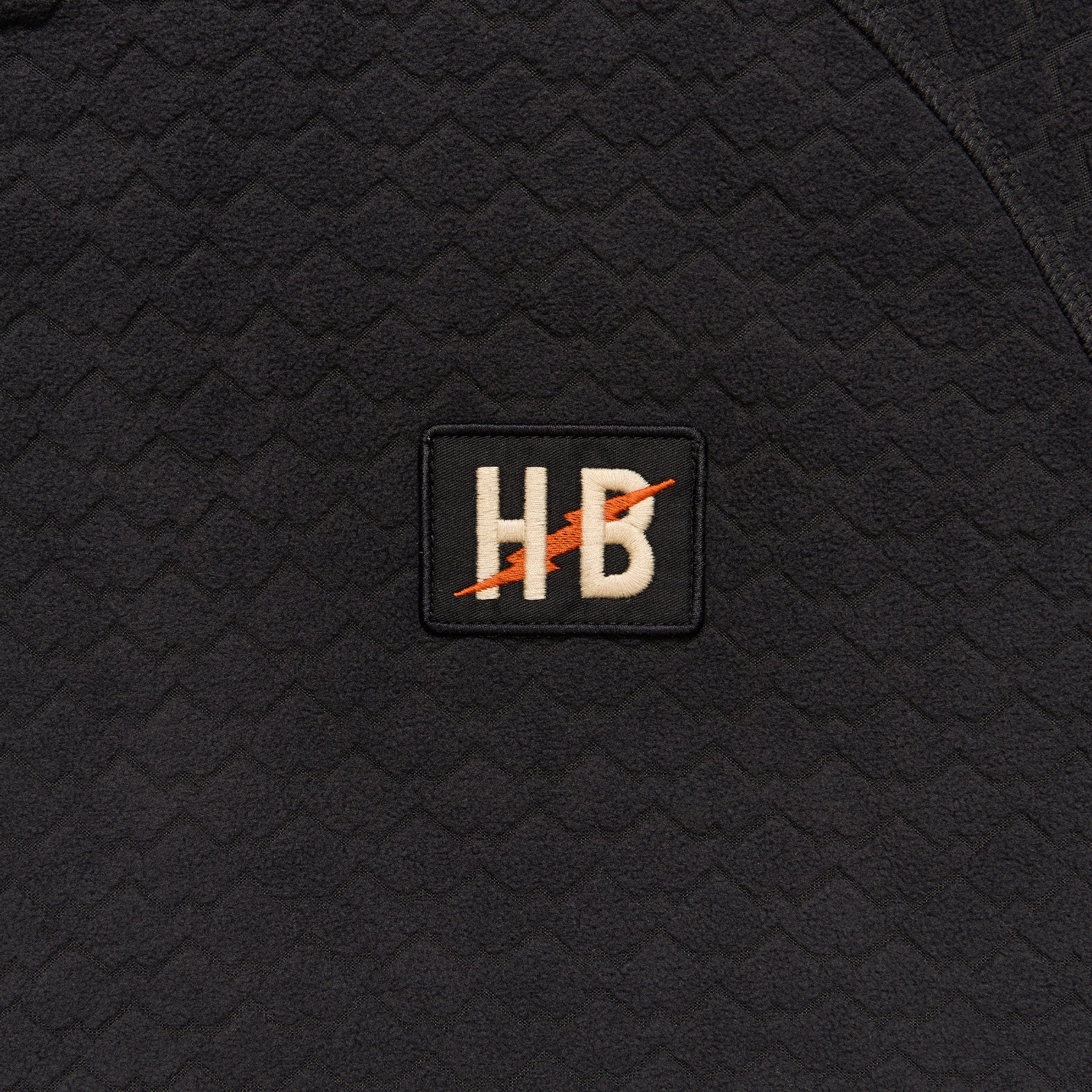 Black textured fabric with a logo patch featuring 'HB' on it.
