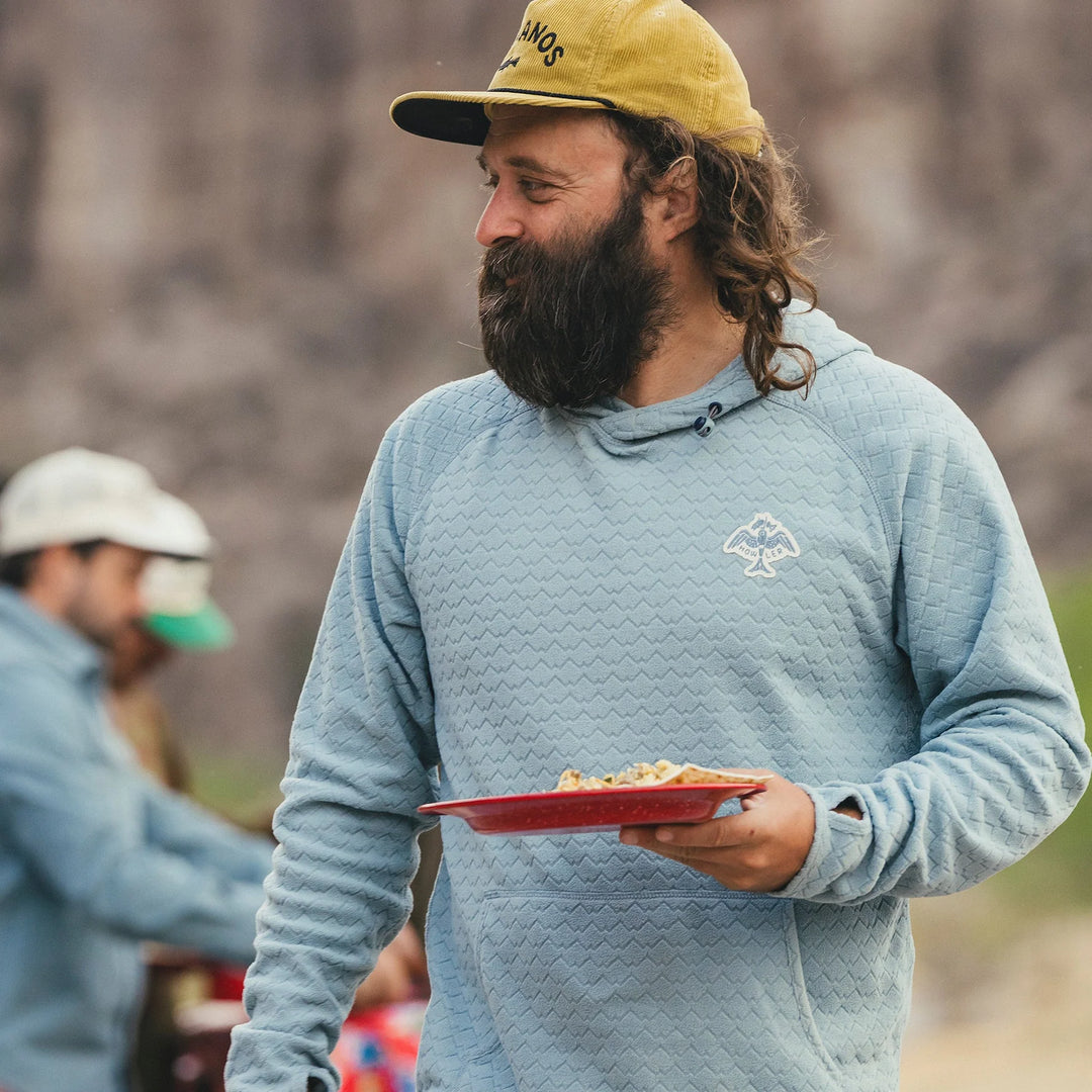 Man in a blue jacket and yellow cap holding a red plate outdoors