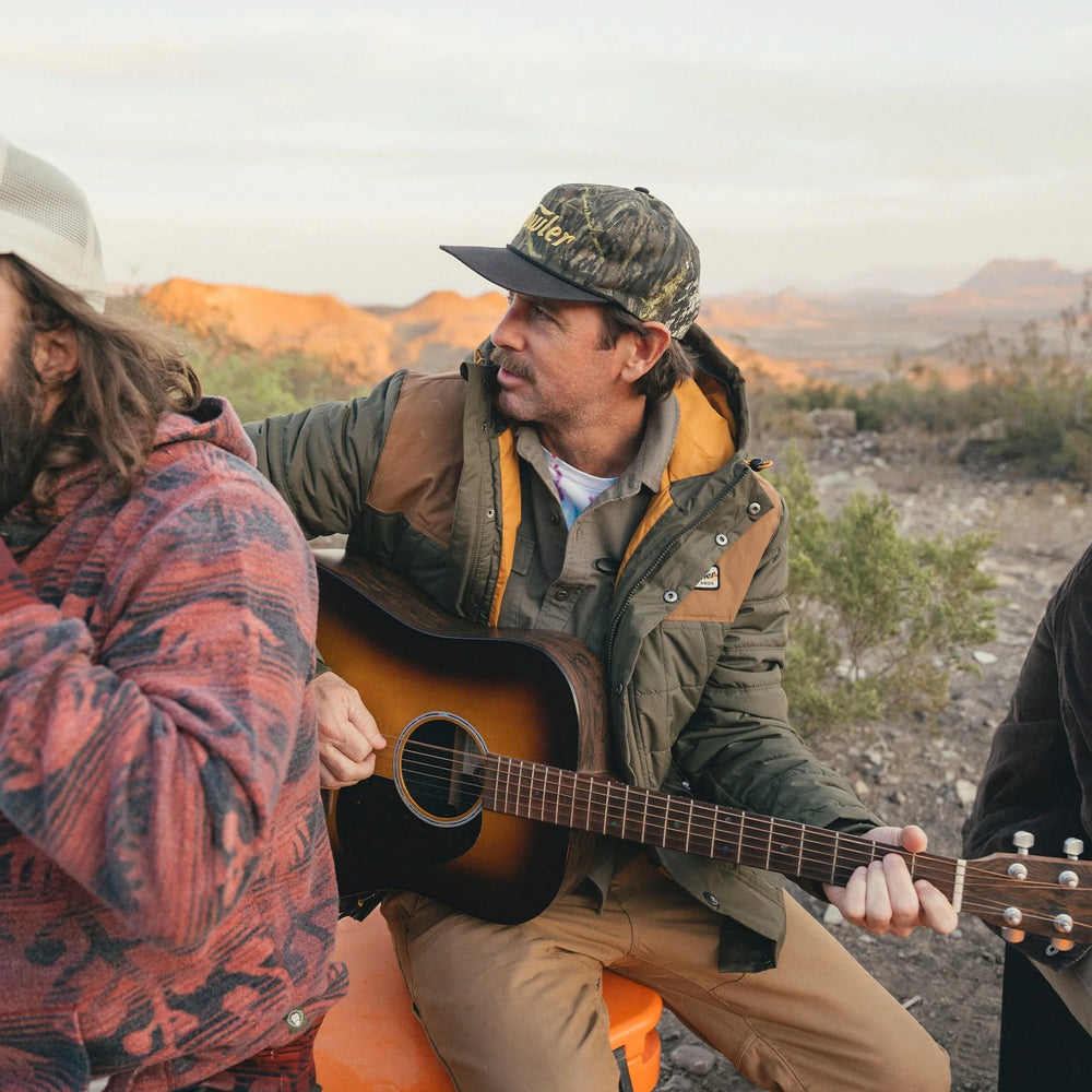 Two men playing guitar outdoors with a scenic background