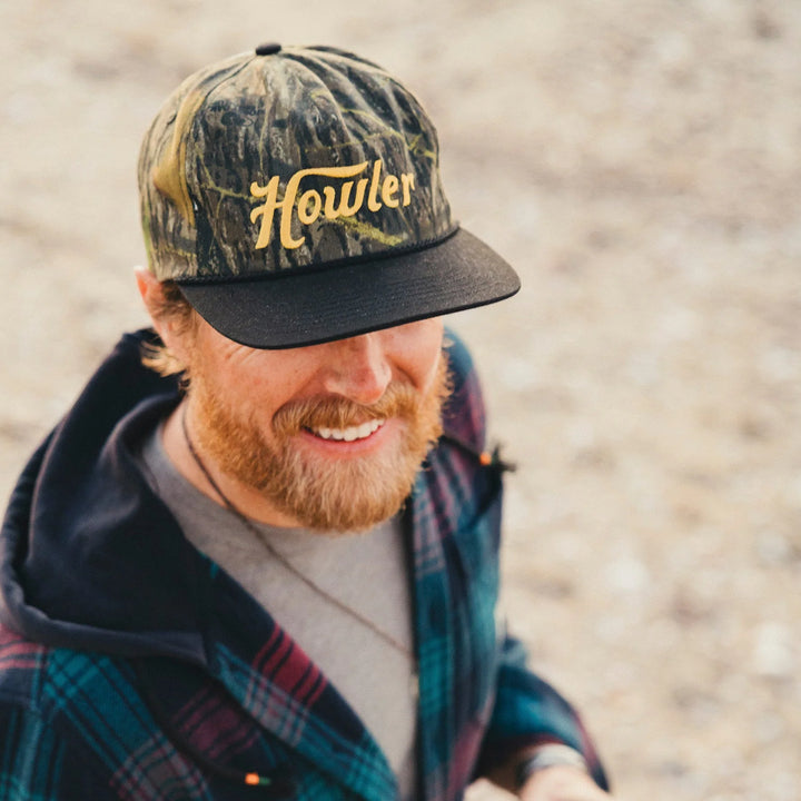 Man wearing a camouflage cap with 'Howler' branding outdoors
