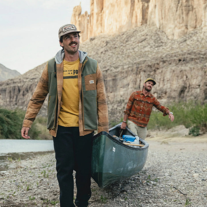 Two men carrying a canoe by a body of water with cliffs in the background