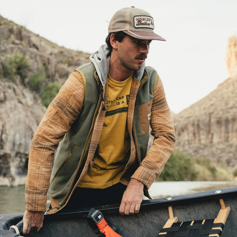 Man in outdoor setting with mountains, wearing a cap and jacket.