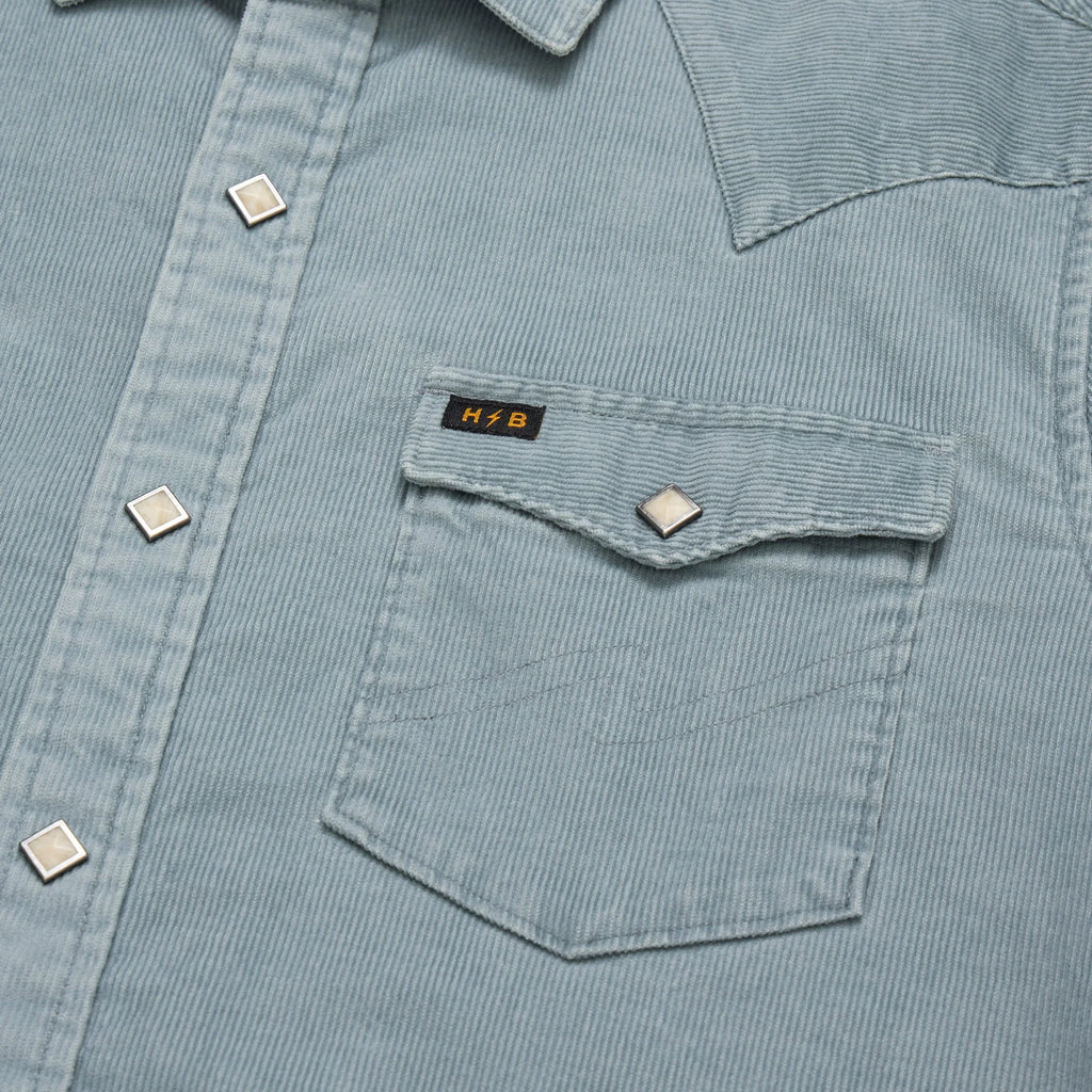 Close-up of a light blue corduroy shirt with a pocket and visible brand logo.