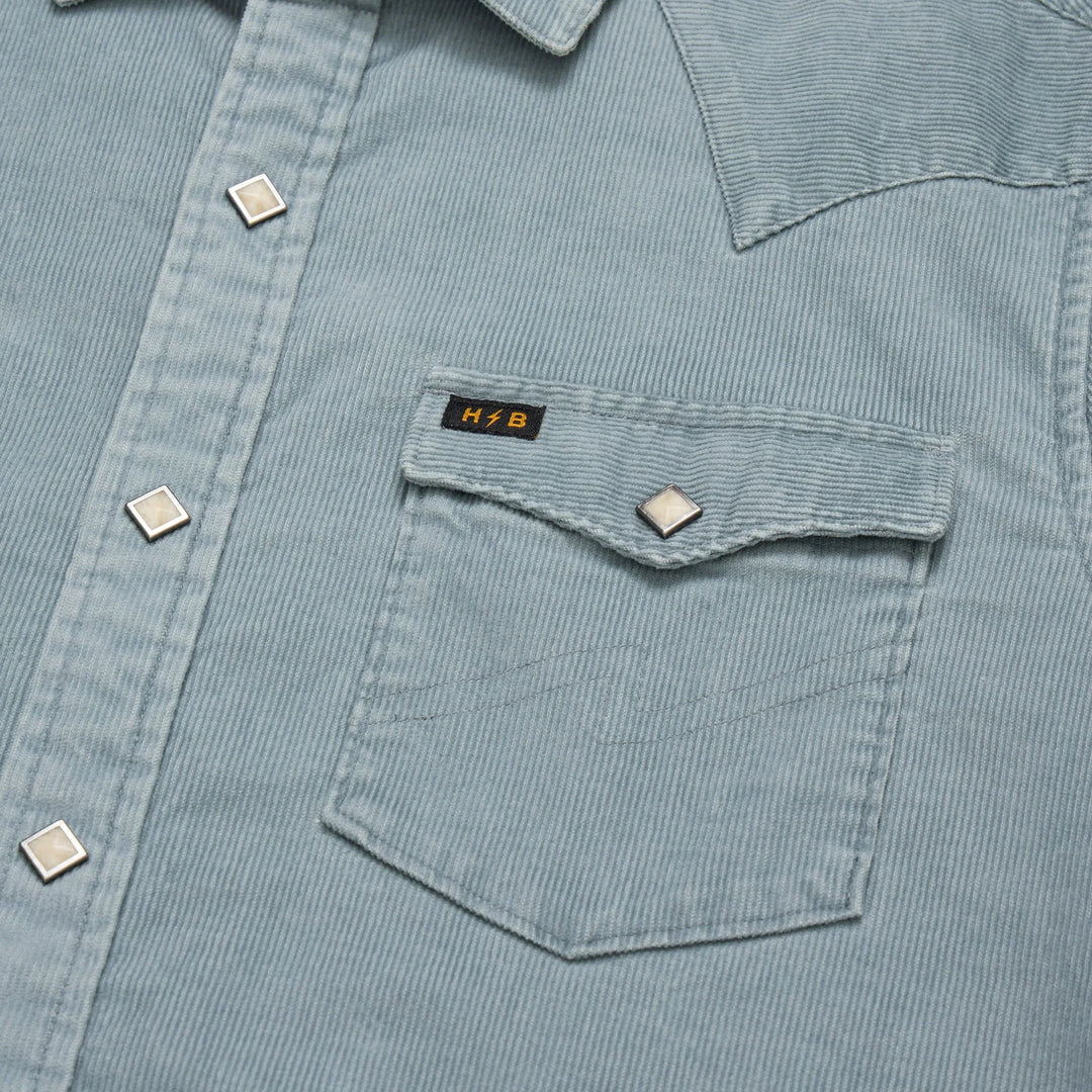 Close-up of a light blue corduroy shirt with a pocket and visible brand logo.