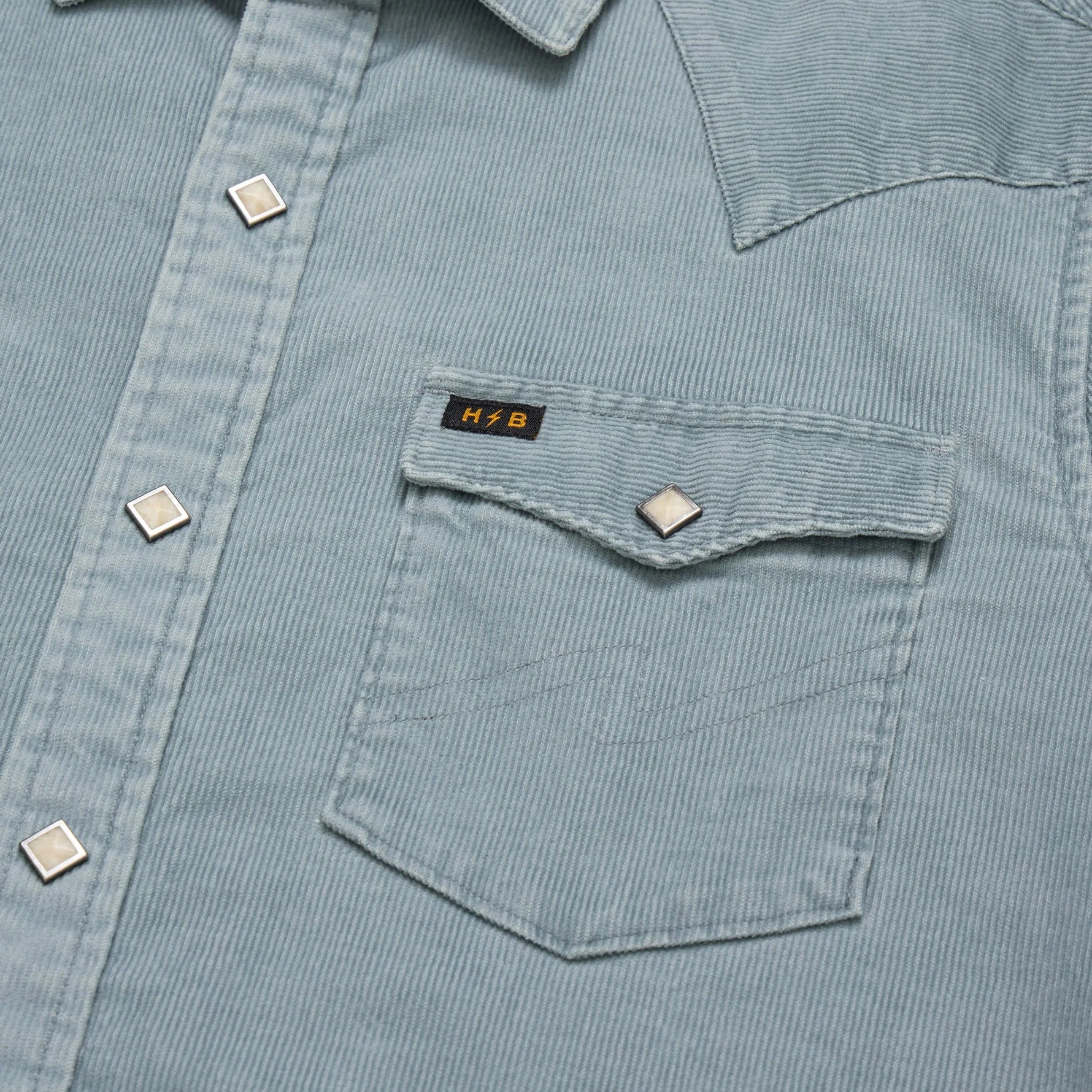 Close-up of a light blue corduroy shirt with a pocket and visible brand logo.