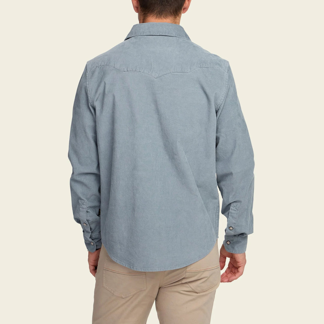 Person wearing a light blue button-up shirt and beige pants on a beige background