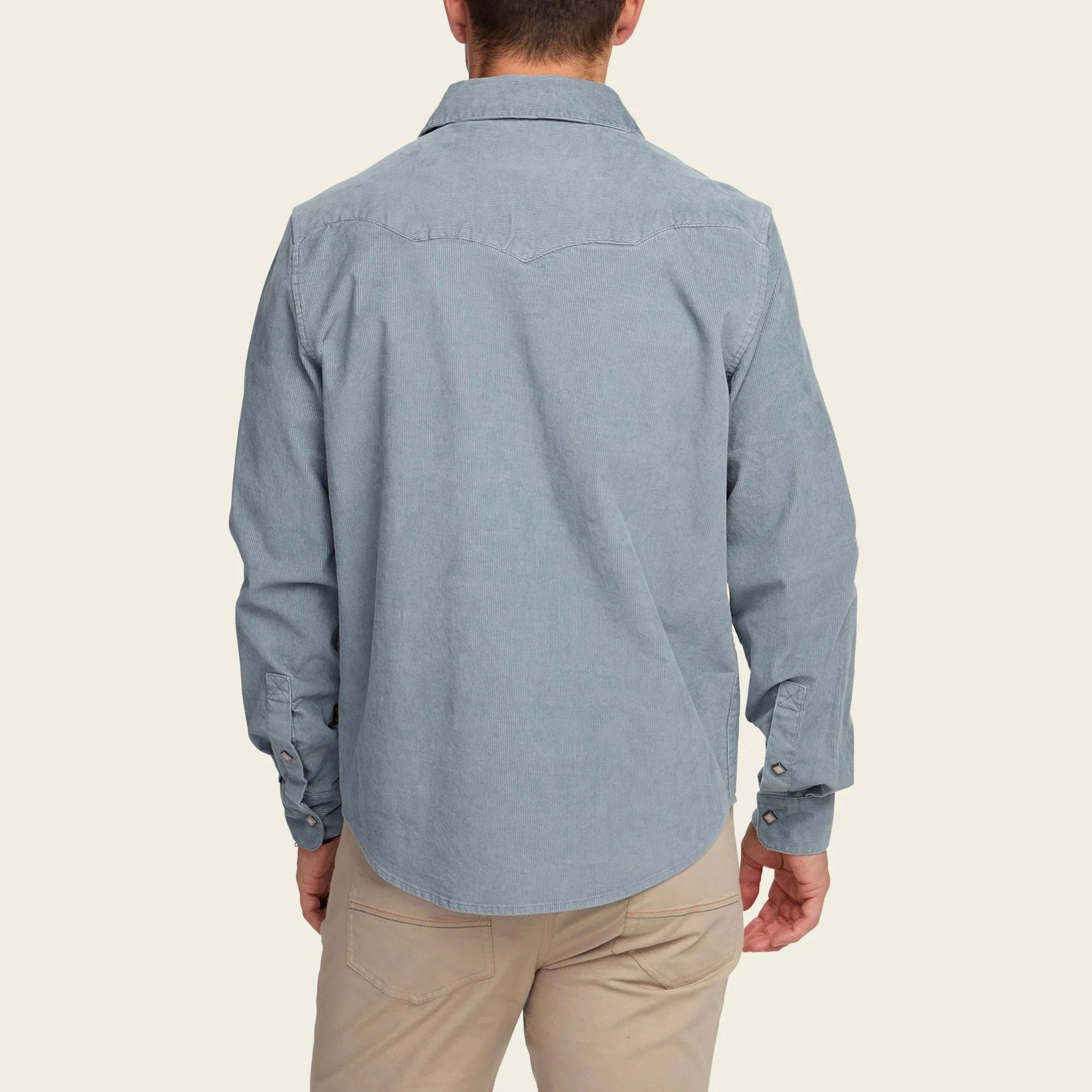 Person wearing a light blue button-up shirt and beige pants on a beige background