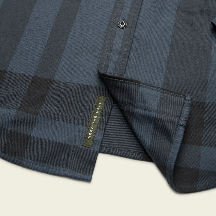 Close-up of a navy checkered shirt with a brand label on a light background
