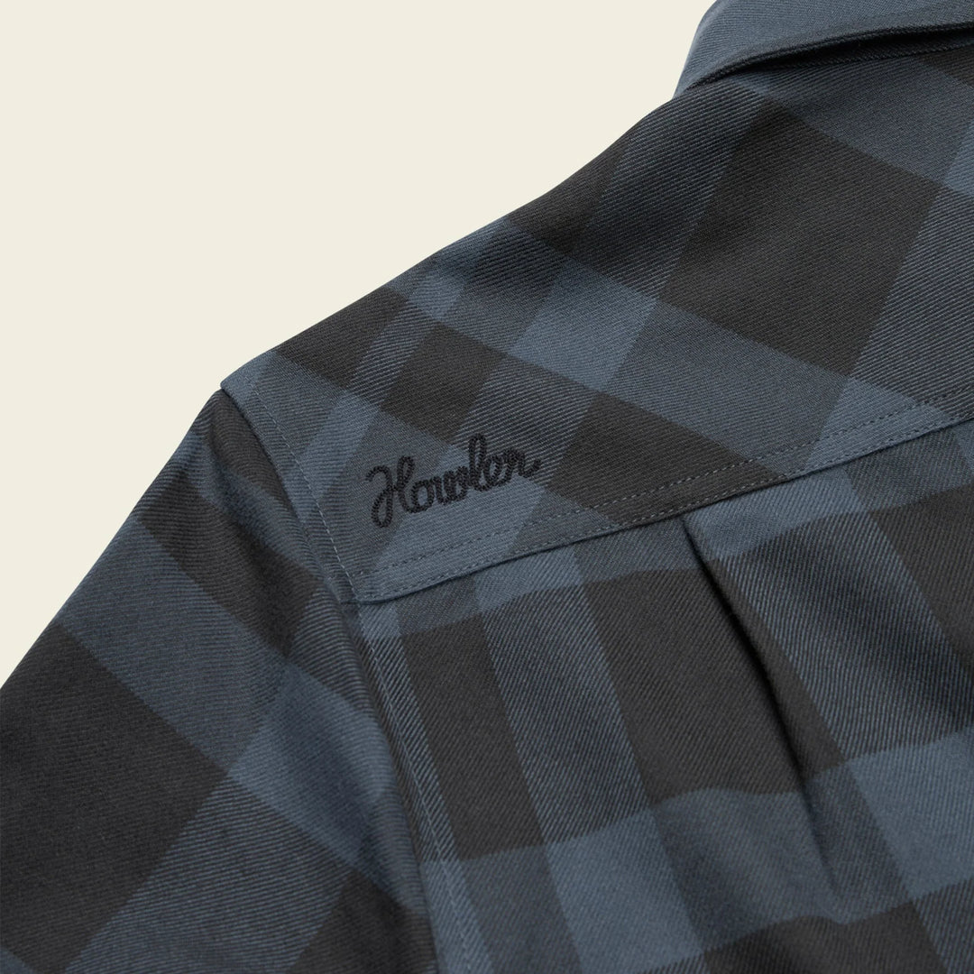 Close-up of a checkered shirt with 'Howler' branding on a beige background