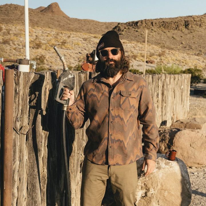 Man with beard and sunglasses holding a gun in a desert setting