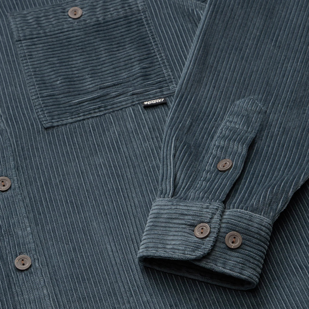 Close-up of a blue corduroy shirt with a brand label on the chest pocket.