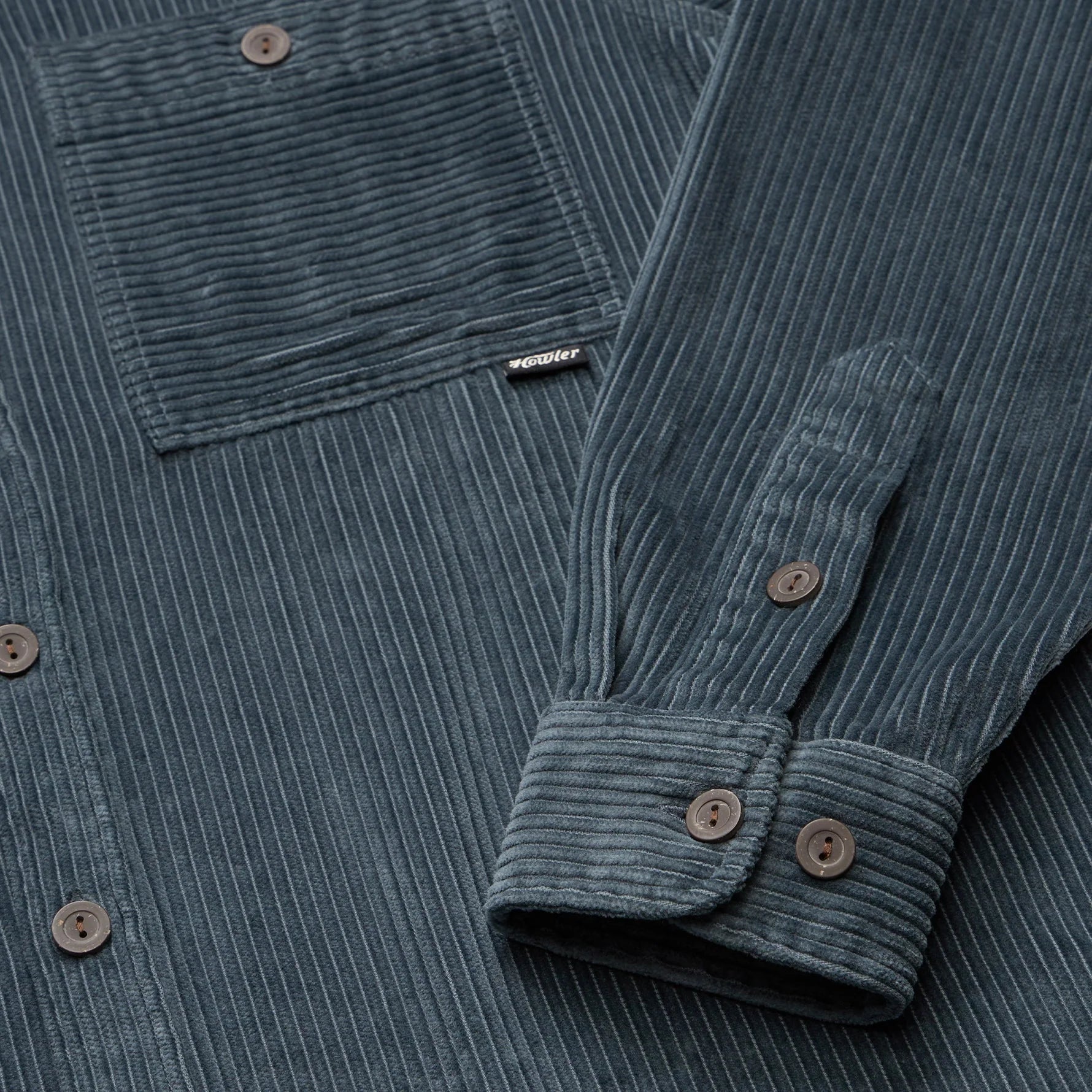 Close-up of a blue corduroy shirt with a brand label on the chest pocket.