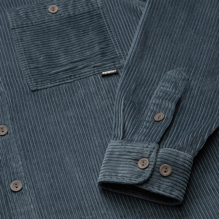 Close-up of a blue corduroy shirt with a brand label on the chest pocket.