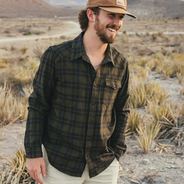 Man wearing a plaid shirt and cap standing in a desert landscape