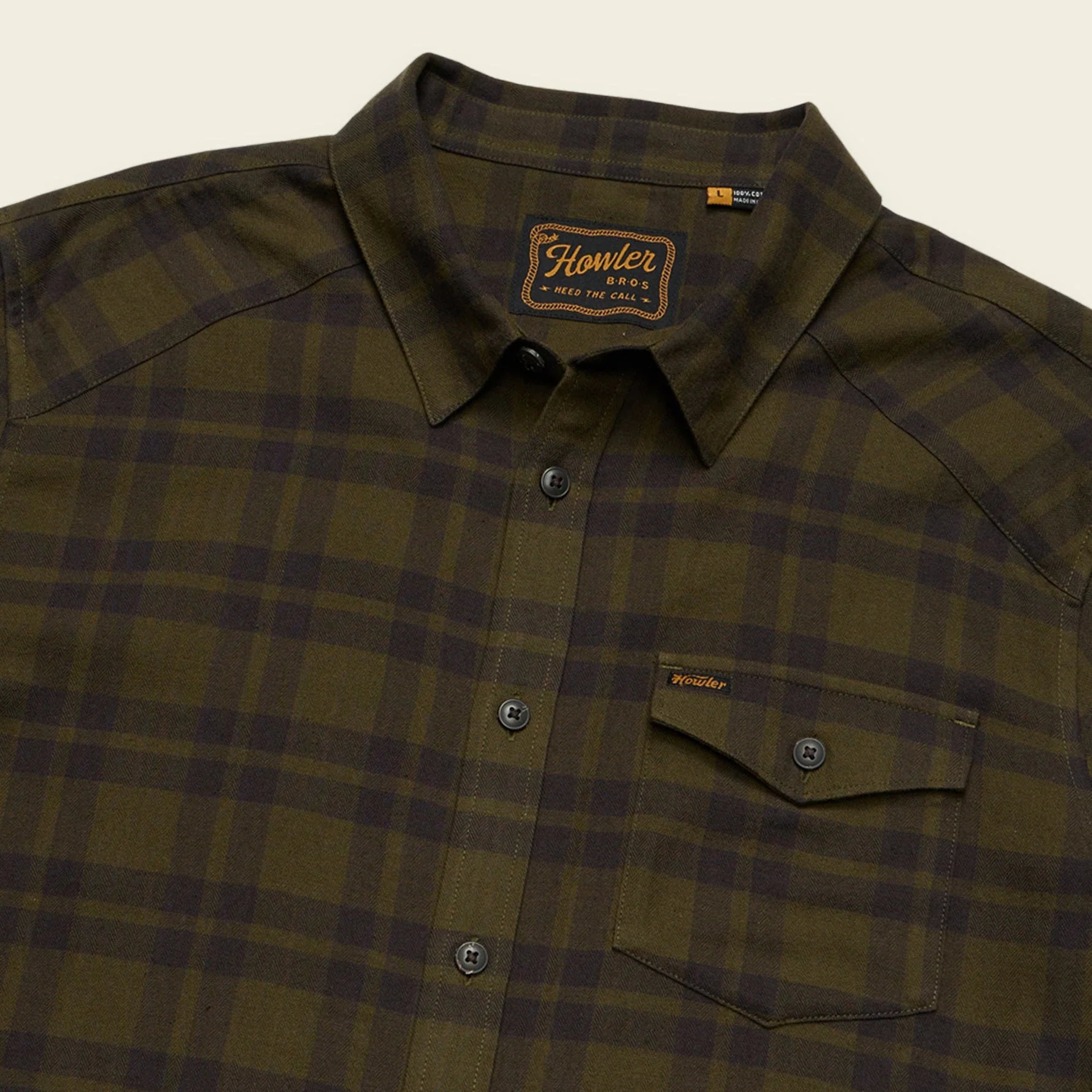Green Howler Brothers plaid shirt with a brand logo on a beige background