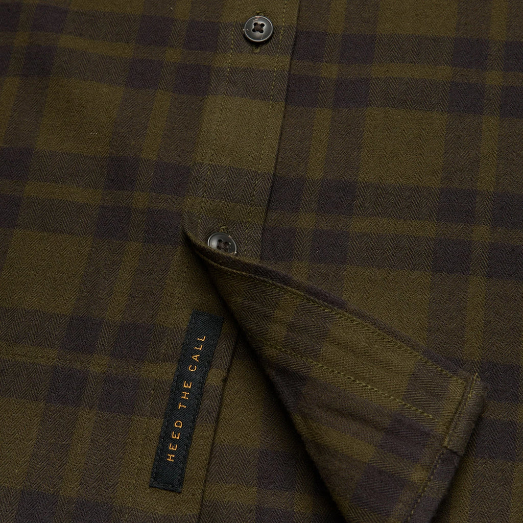 Close-up of a Howler Brothers plaid shirt with a brand label on a dark background