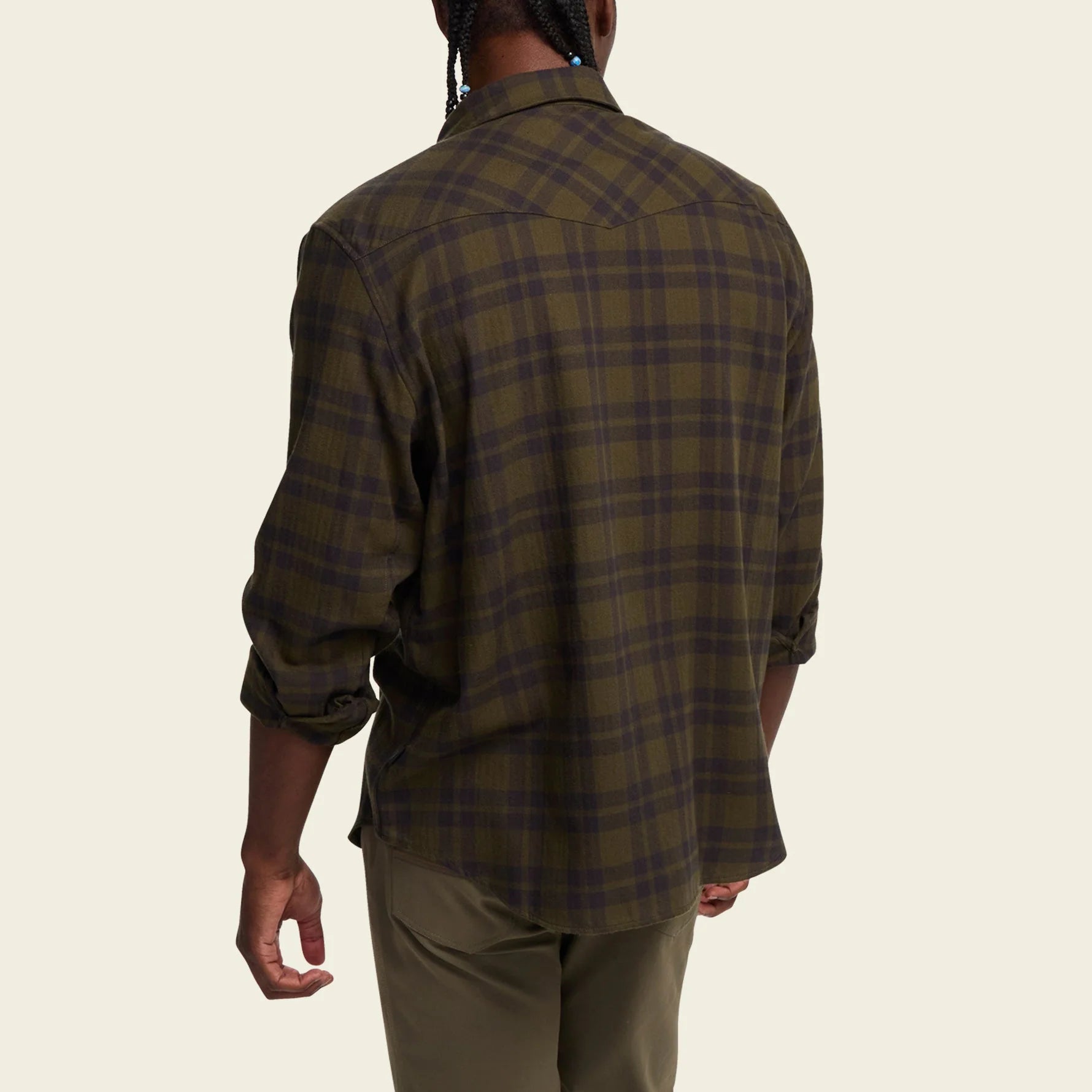 Person wearing a Howler Brothers green plaid shirt on a beige background