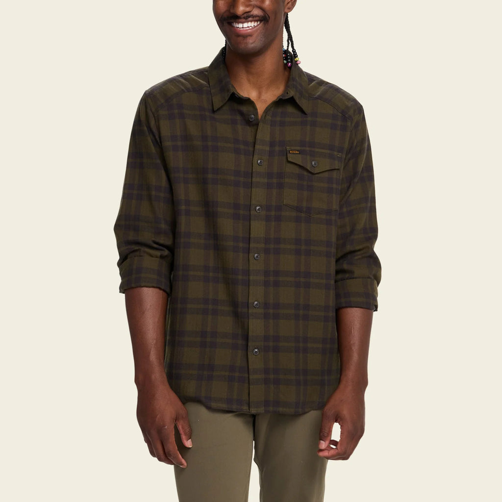 Man wearing a green Howler Brothers plaid shirt on a beige background