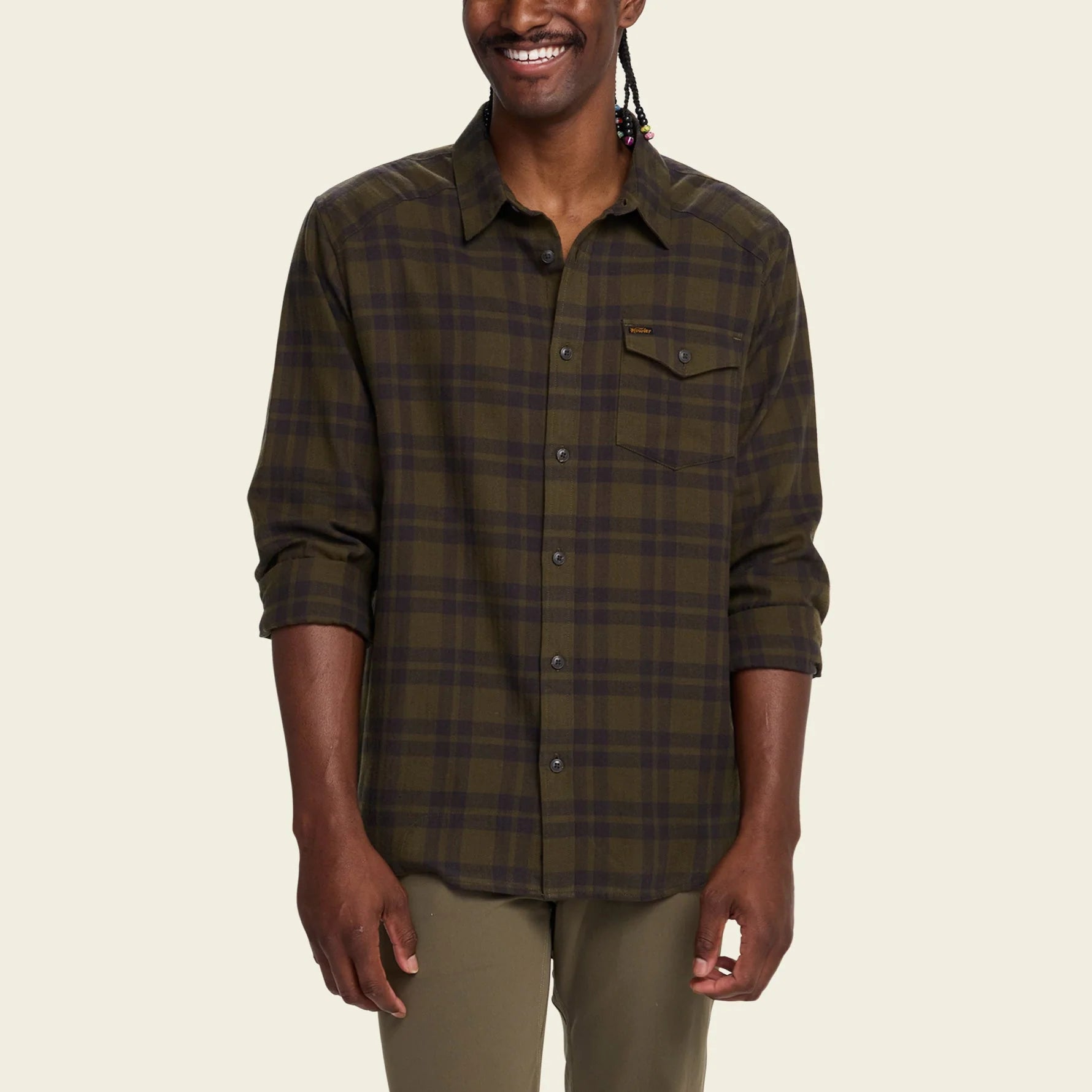 Man wearing a green Howler Brothers plaid shirt on a beige background