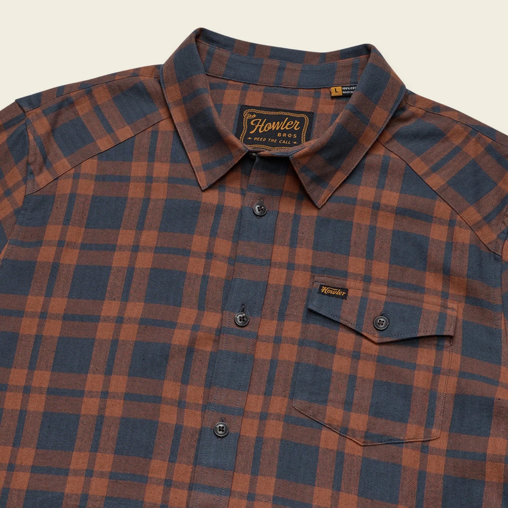 Howler Brothers plaid shirt with visible brand logo on a beige background
