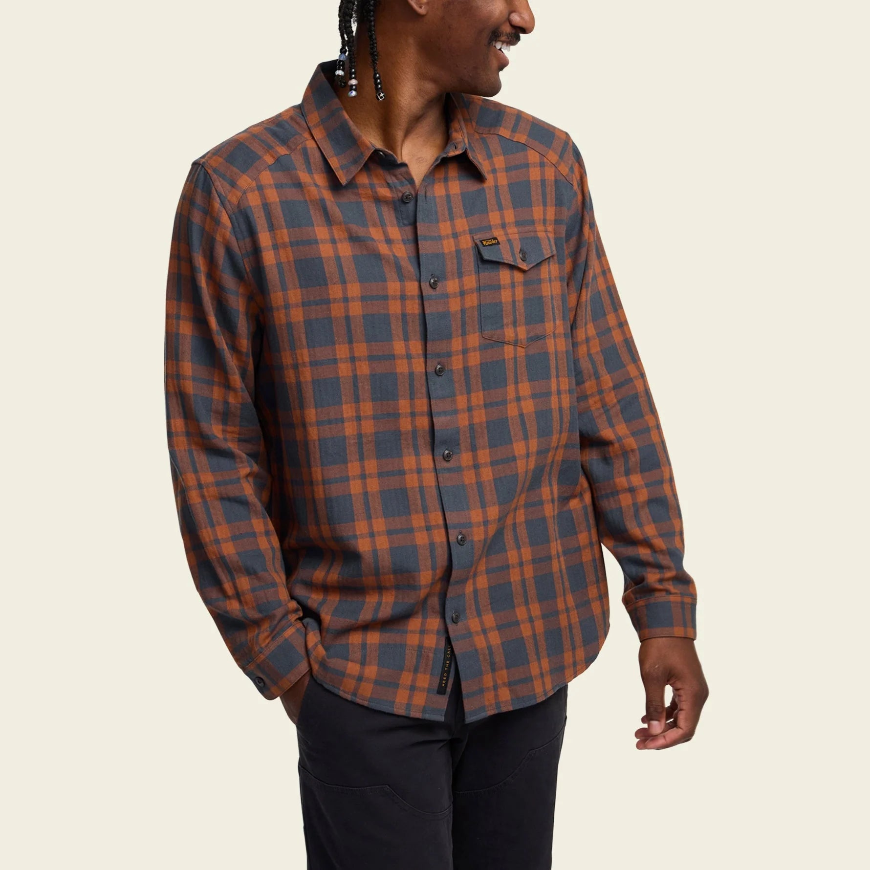 Person wearing a Howler Brothers plaid shirt on a beige background