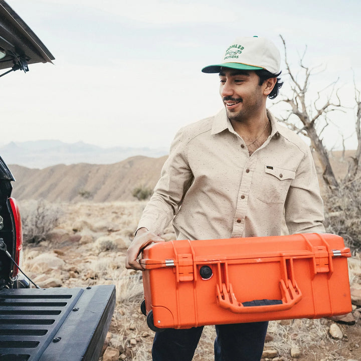 Man holding an orange case in a desert setting with mountains in the background