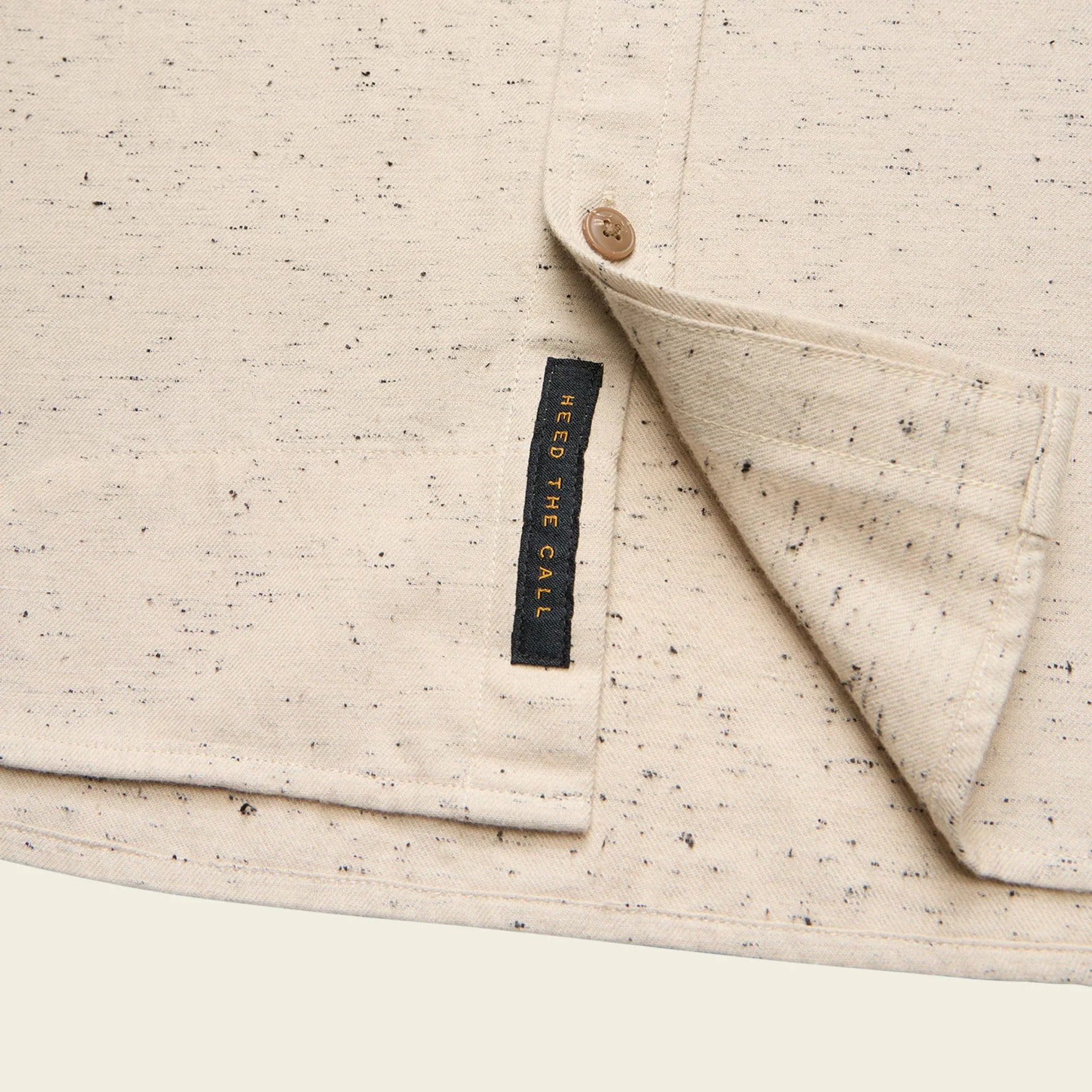 Close-up of a beige textured fabric with a button and 'Need The Call' label.