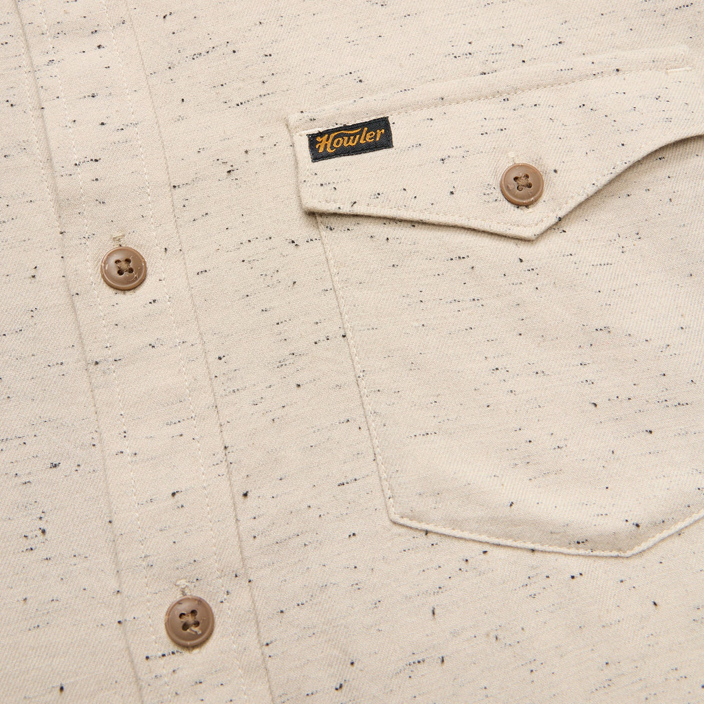 Close-up of a speckled Howler Brothers shirt with buttons and a brand label on a beige background
