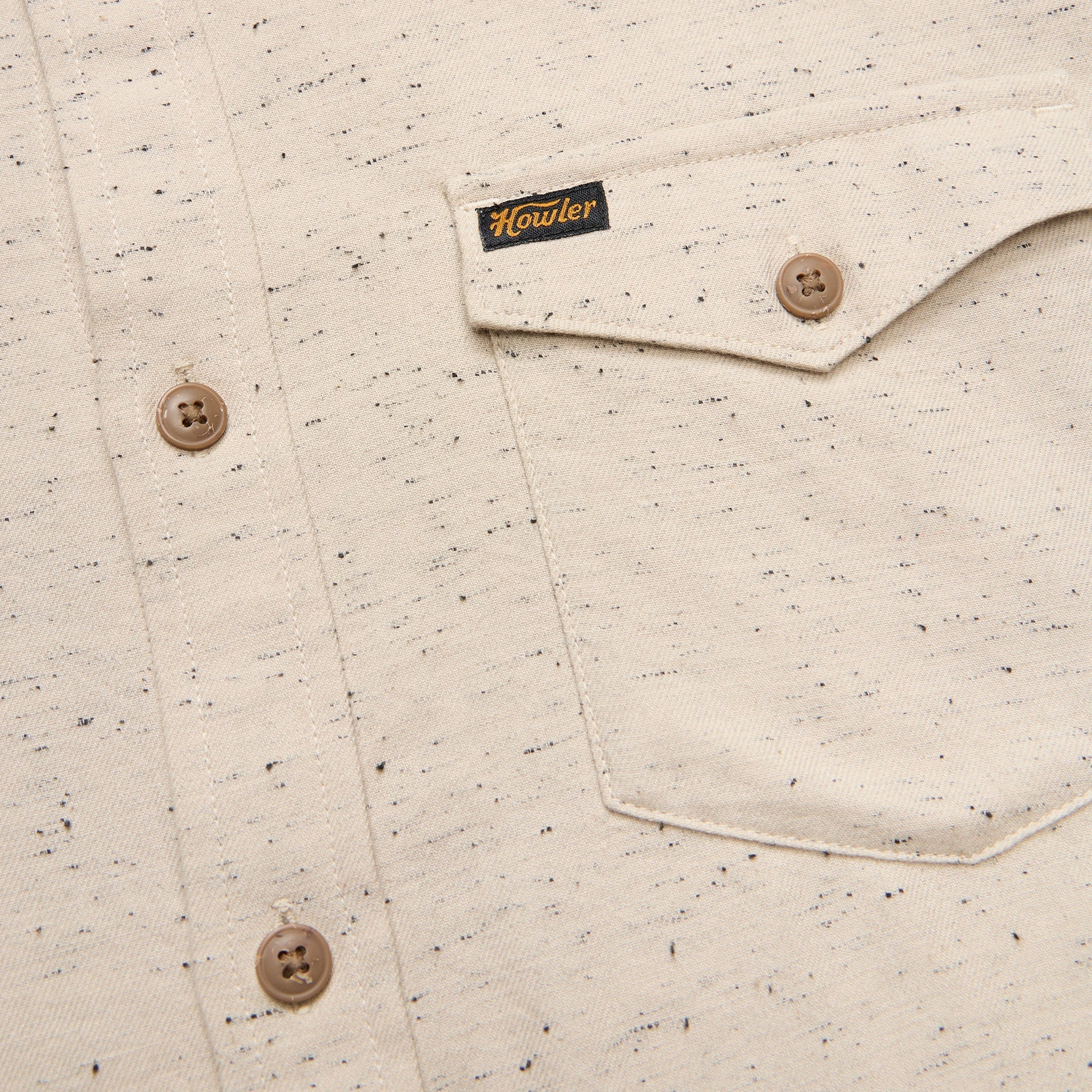 Close-up of a speckled Howler Brothers shirt with buttons and a brand label on a beige background