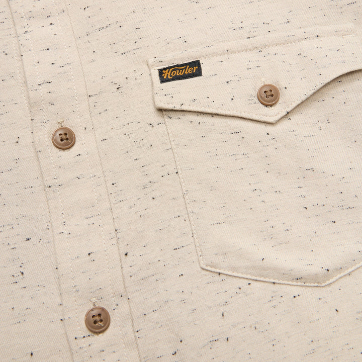 Close-up of a speckled shirt with buttons and a brand label on a beige background