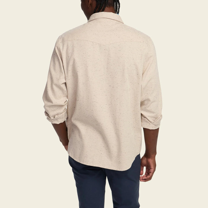 Person wearing a beige shirt and dark pants on a plain background
