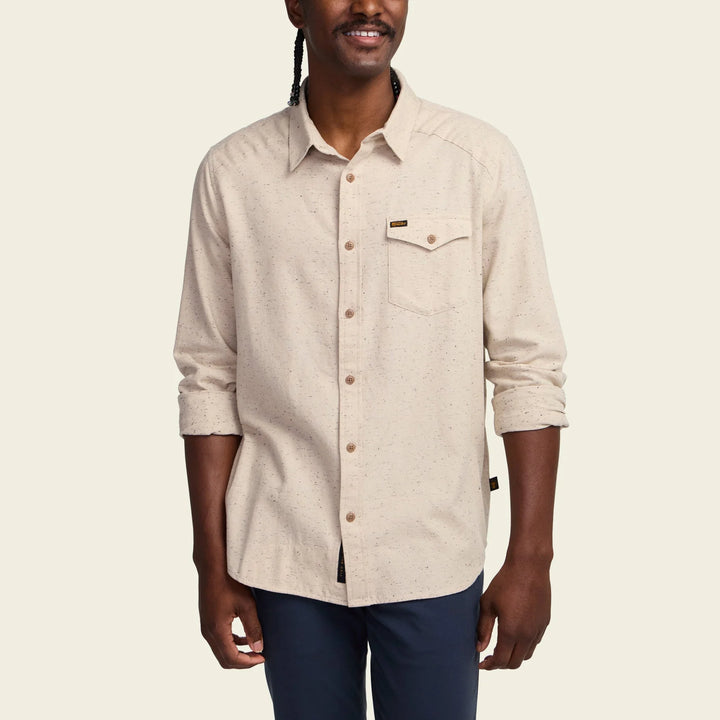 Man wearing a beige button-up shirt with a visible brand logo on a plain background