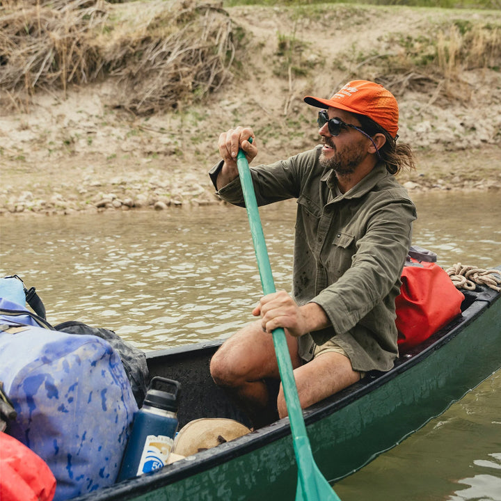 Man paddling a canoe on a river with a scenic background