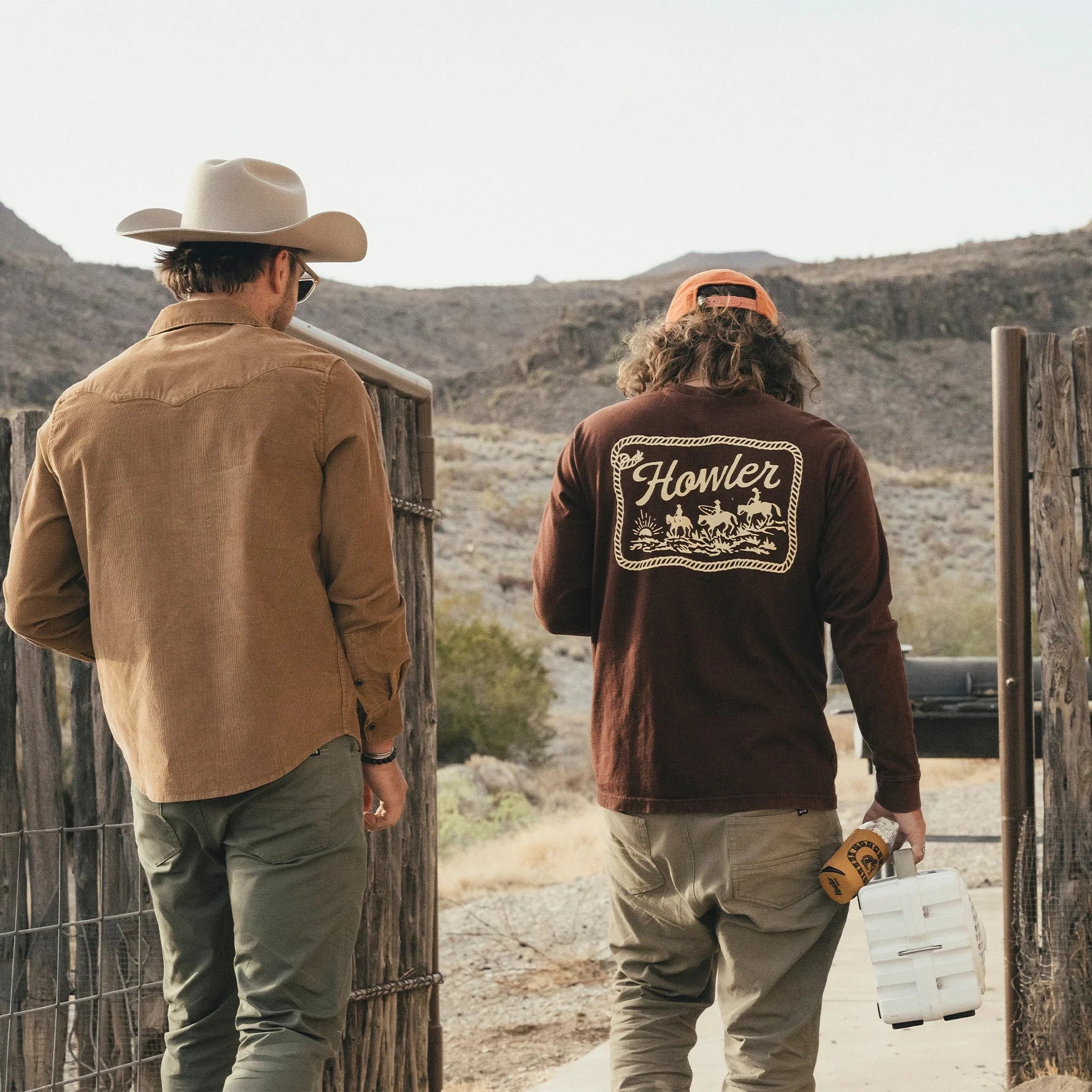 Two men in a desert setting, one wearing a cowboy hat and the other a 'Howler' branded shirt.