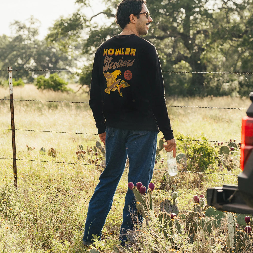 Man wearing a black sweatshirt with 'Howler Brothers' logo in a field with cacti and a truck in the background.